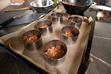Two rows of metallic forms filled with fried minced meat with chopped vegetables
