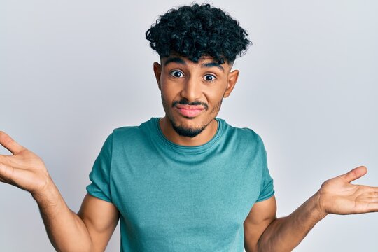 Young arab handsome man wearing casual clothes clueless and confused expression with arms and hands raised. doubt concept.