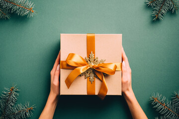 Vintage Christmas gift box with golden ribbon bow and snowflake on dark green background with fir tree branches. Retro style Xmas present, New Year surprise.