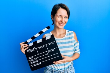 Young brunette woman with short hair holding video film clapboard winking looking at the camera...