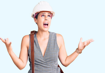 Young beautiful woman wearing architect hardhat and leather bag crazy and mad shouting and yelling...