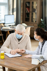Obraz premium Sick senior male patient in mask and casualwear signing medical paper