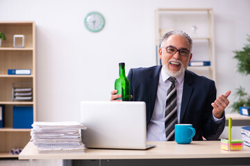 Naklejka premium Old male employee drinking alcohol in the office