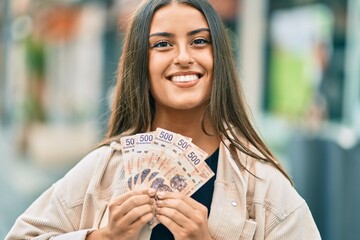 Young hispanic girl smiling happy holding mexican 500 pesos banknotes at the city.