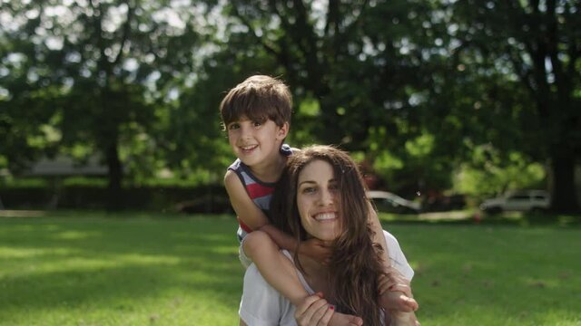 Portrait of a beautiful young mother with her son sitting on her shoulders at the park