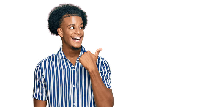 African american man with afro hair wearing casual clothes smiling with happy face looking and pointing to the side with thumb up.