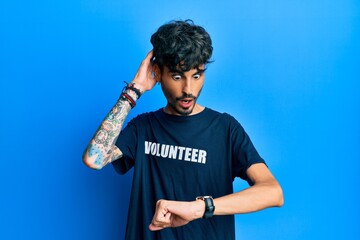 Young hispanic man wearing volunteer t shirt looking at the watch time worried, afraid of getting late