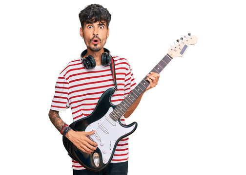 Young hispanic man playing electric guitar scared and amazed with open mouth for surprise, disbelief face