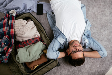 Young smiling man packing clothes into travel bag. Man preparing for the trip..