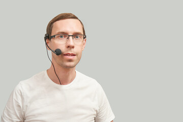 Men in call center. White t-shirt. Headset for telemarketing. Male manager helps customer. Phone operator. Studio portrait. Person multi language translator. Grey background.