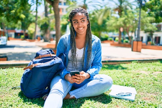 Young african american student woman smiling happy using smartphone sitting on the grass at the university campus
