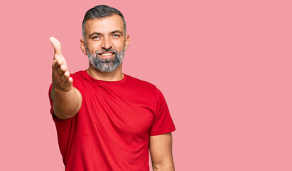 Fototapeta premium Middle age handsome man wearing casual clothes smiling friendly offering handshake as greeting and welcoming. successful business.