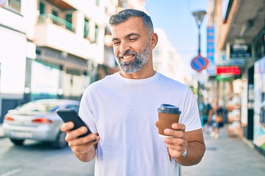 Middle age grey-haired man using smartphone and drinking take away coffee at the city