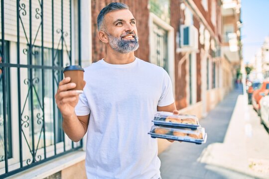 Middle age grey-haired man smiling happy holding cup of coffee and take away food at the city.