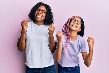 Beautiful african american mother and daughter wearing casual clothes and glasses very happy and excited doing winner gesture with arms raised, smiling and screaming for success. celebration concept.