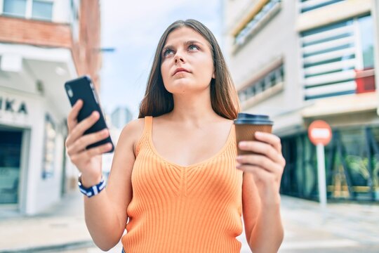Young middle east gir with serious expression using smartphone and drinking coffee at the city.