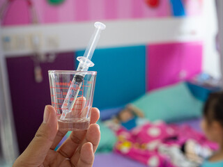 Focus medicine with syringe in glass for the patient and boy sleeping on the bed in hospital room background. Patient treatment and healthcare concept.