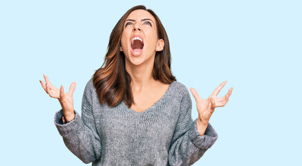 Fototapeta na wymiar Young brunette woman wearing casual winter sweater crazy and mad shouting and yelling with aggressive expression and arms raised. frustration concept.