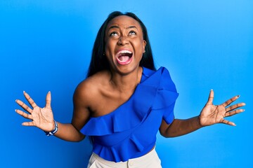 Young african woman wearing casual clothes over blue background crazy and mad shouting and yelling with aggressive expression and arms raised. frustration concept.