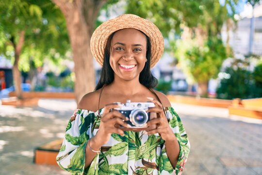 Young african american tourist woman on vacation smiling happy using vintage camera at the city.