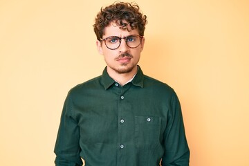 Young caucasian man with curly hair wearing casual clothes and glasses skeptic and nervous, frowning upset because of problem. negative person.