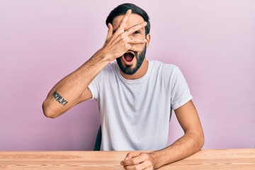 Young hispanic man with beard wearing casual clothes sitting on the table smiling with hands on chest, eyes closed with grateful gesture on face. health concept.