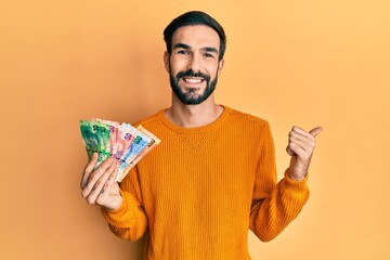 Young hispanic man with beard holding south african rand banknotes screaming proud, celebrating victory and success very excited with raised arm