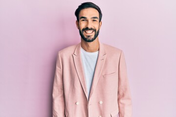 Young hispanic man with beard wearing pink elegant jacket doing ok gesture with hand smiling, eye looking through fingers with happy face.