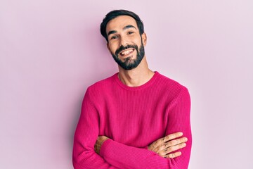 Young hispanic man with beard wearing casual winter sweater smiling and looking at the camera pointing with two hands and fingers to the side.