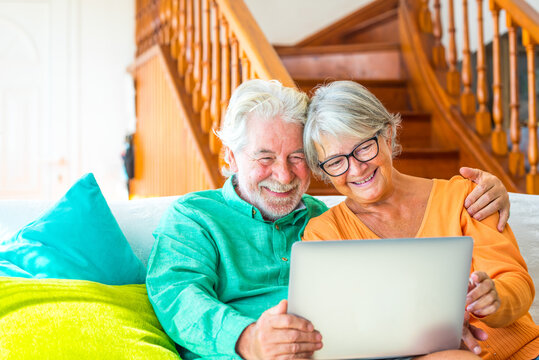 couple of two happy mature and old people or seniors at home sitting on the sofa enjoying and having fun together looking and using a laptop or computer pc - Powered by Adobe