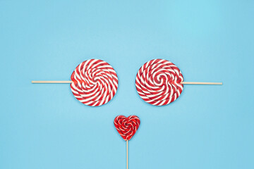 Christmas funny face made of candy red lollipops on blue background. Merry Christmas sweets and Happy New Year concept