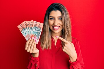 Beautiful brunette woman holding australian 20 dollars smiling happy pointing with hand and finger