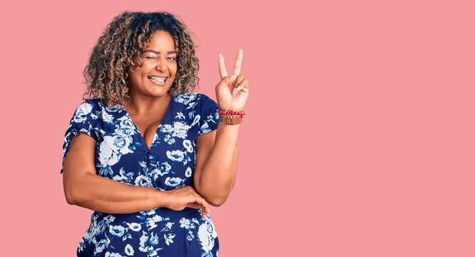 Young african american plus size woman wearing casual clothes smiling with happy face winking at the camera doing victory sign. number two.