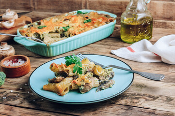 Casserole with pasta, mushrooms, broccoli sauce and cheese on a rustic wooden background.