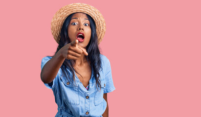 Young indian girl wearing summer hat pointing displeased and frustrated to the camera, angry and furious with you