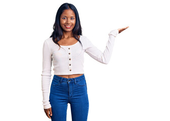 Young indian girl wearing casual clothes smiling cheerful presenting and pointing with palm of hand looking at the camera.