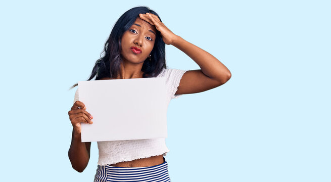 Young indian girl holding blank empty banner stressed and frustrated with hand on head, surprised and angry face