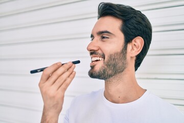 Young hispanic man smiling happy sending audio message using smartphone at city.