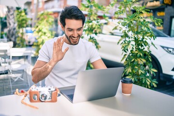 Young hispanic man smiling happy working using laptop at coffee shop terrace.