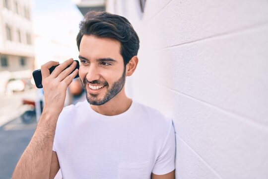 Young hispanic man smiling happy listening audio message using smartphone at city.