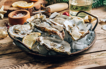 Oysters with lemon on a vintage dish on a rustic wooden background with a festive decor. Christmas dinner.