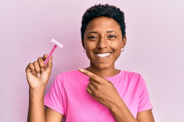 African american woman with short hair holding razor scared and amazed with open mouth for surprise, disbelief face