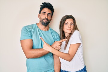 Beautiful young couple of boyfriend and girlfriend together pointing to both sides with fingers, different direction disagree