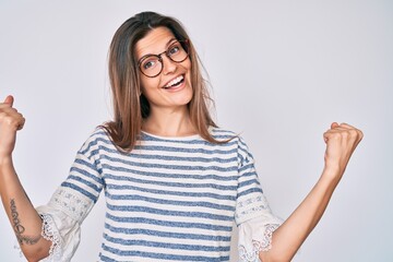 Beautiful caucasian woman wearing casual clothes and glasses screaming proud, celebrating victory and success very excited with raised arms