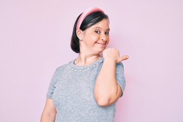 Obraz na płótnie Canvas Brunette woman with down syndrome wearing casual clothes smiling with happy face looking and pointing to the side with thumb up.