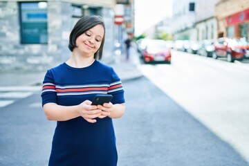 Beautiful brunette woman with down syndrome at the town on a sunny day using smartphone