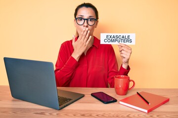 Young brunette woman using laptop holding exascale computers banner covering mouth with hand,...