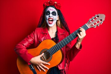 Woman wearing day of the dead costume playing classical guitar angry and mad screaming frustrated and furious, shouting with anger looking up.