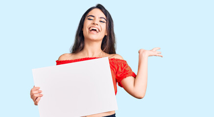 Fototapeta premium Brunette teenager girl holding blank empty banner celebrating victory with happy smile and winner expression with raised hands