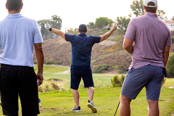 Golfer celebrates swing with friends looking on in the foreground and the golf course in the background